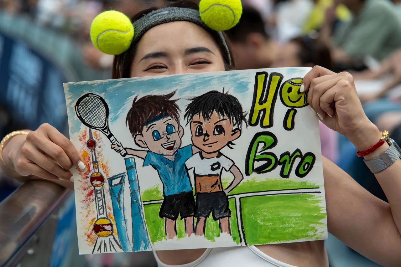 Tennis fan wearing tennis balls and holding a hand-drawn support sign in the stands